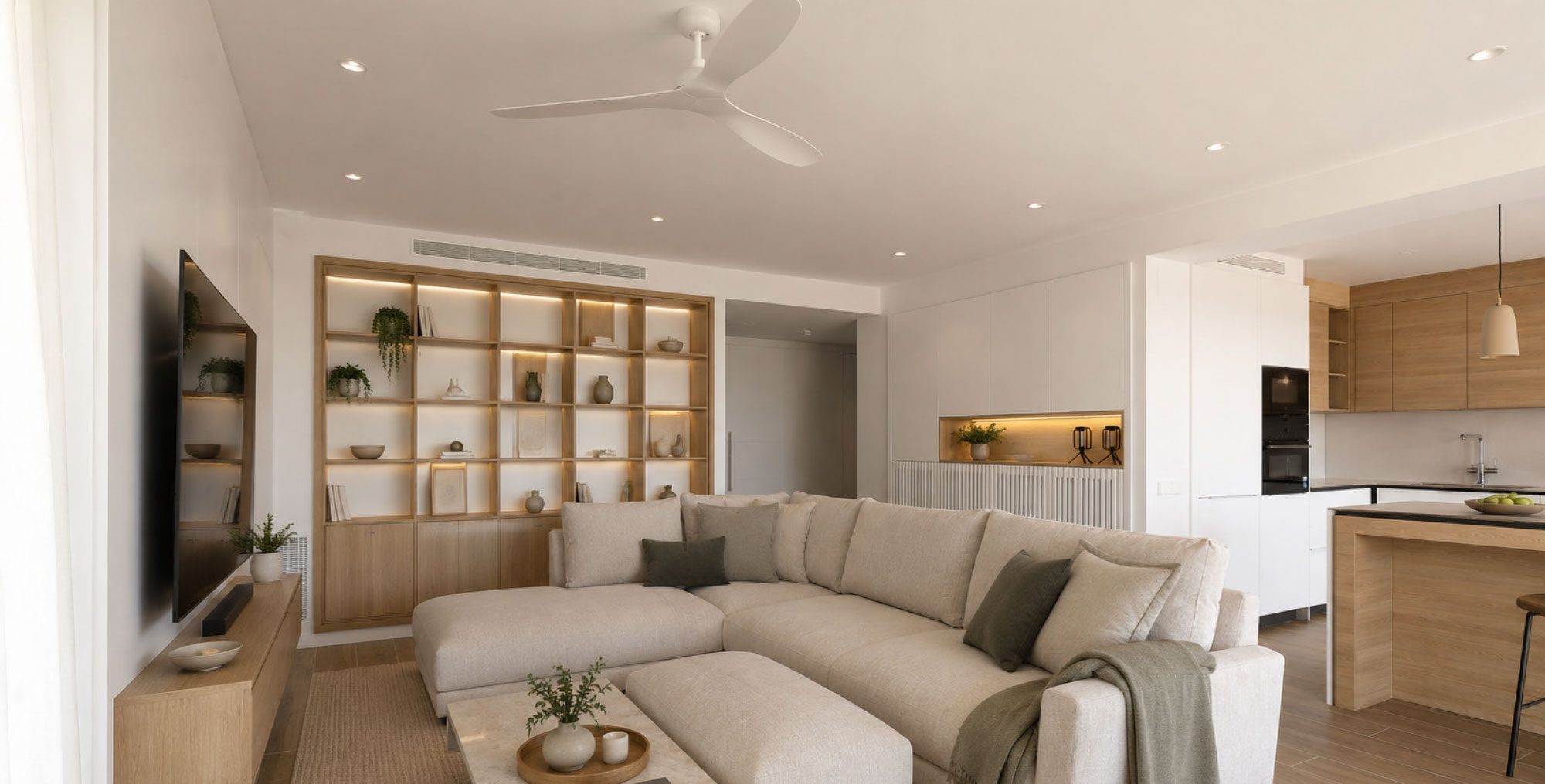 Salón abierto con sofá, librería de madera a medida y cocina al fondo